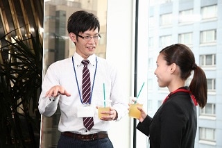 窓際でジュースを飲みながら話すスーツ男女