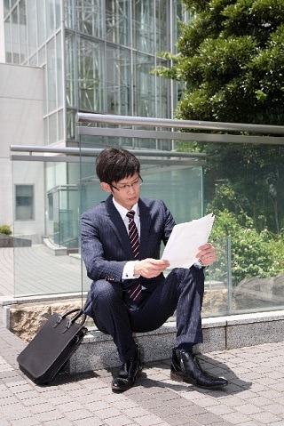 座って資料を読んでいるスーツ男性