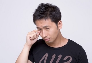 目をこする黒Tシャツの男性