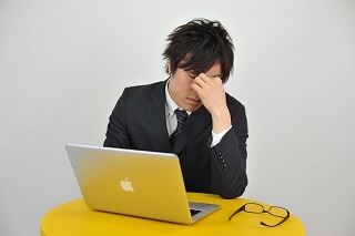 眉間を押さえるスーツ男性