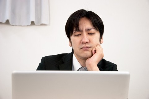 パソコンの前で悩んでいるスーツ男性