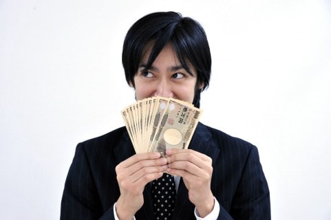 お金を顔の前に出しているスーツ男性