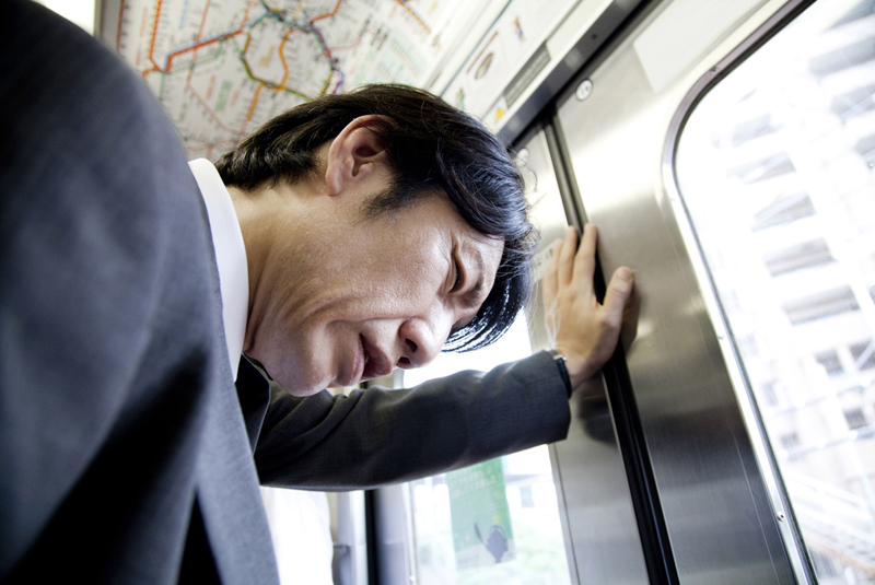 電車でうなだれるスーツ男性