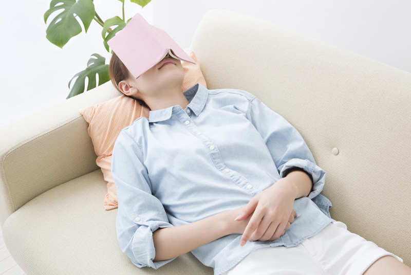 本を顔において寝ている女性