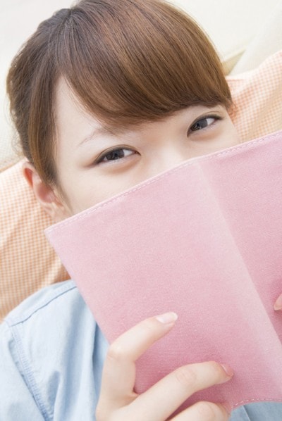 本で顔を隠す女性