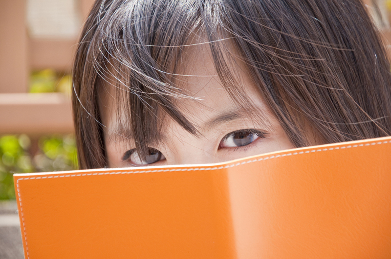 本で顔を隠して目だけ出している女性