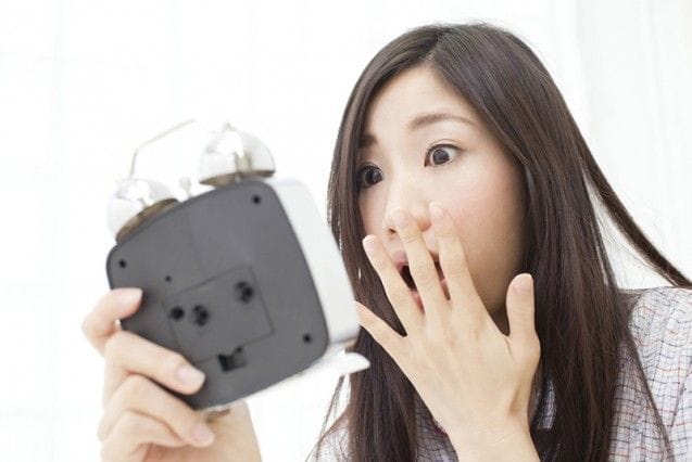 目覚ましを見て驚く女性